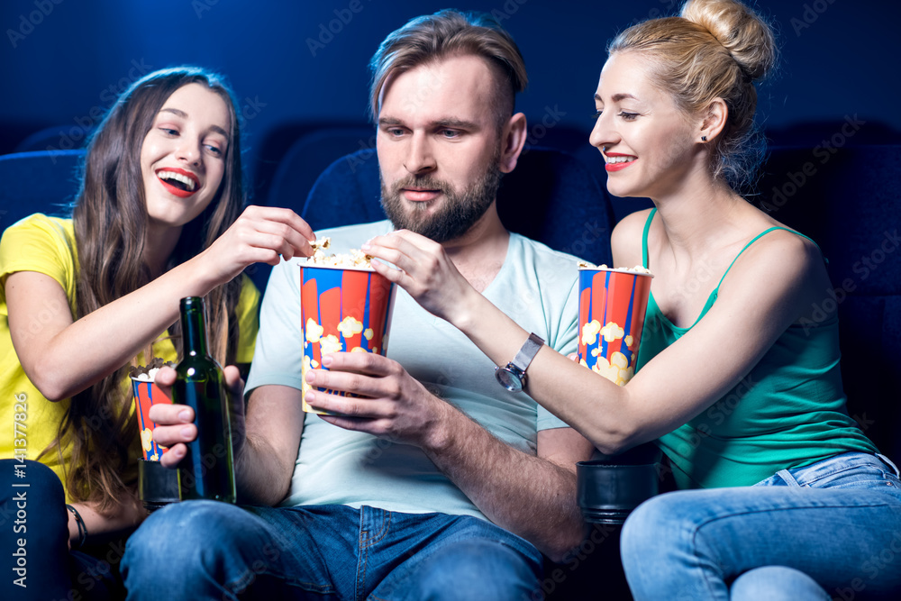 Happy friends watching film sitting together with popcorn in the cinema