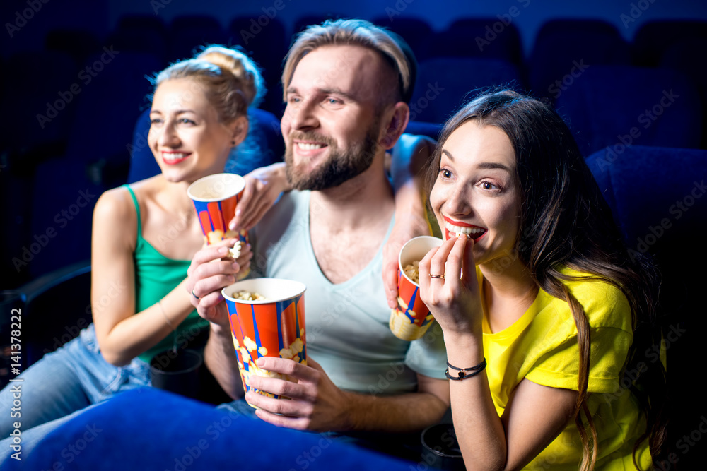 Happy friends watching film sitting together with popcorn in the cinema