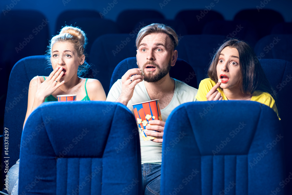 Scared friends watching film sitting together with popcorn in the cinema