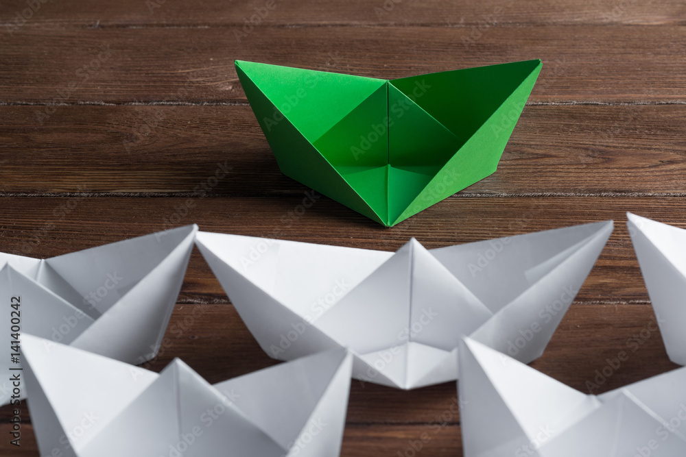 Business leadership concept with white and color paper boats on wooden table