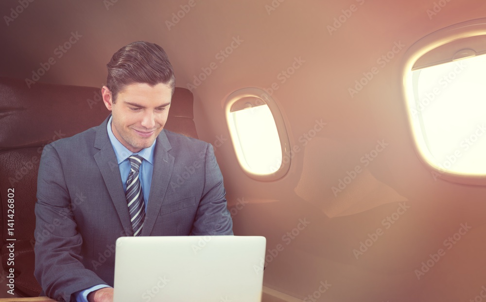 Composite image of happy businessman using laptop at table