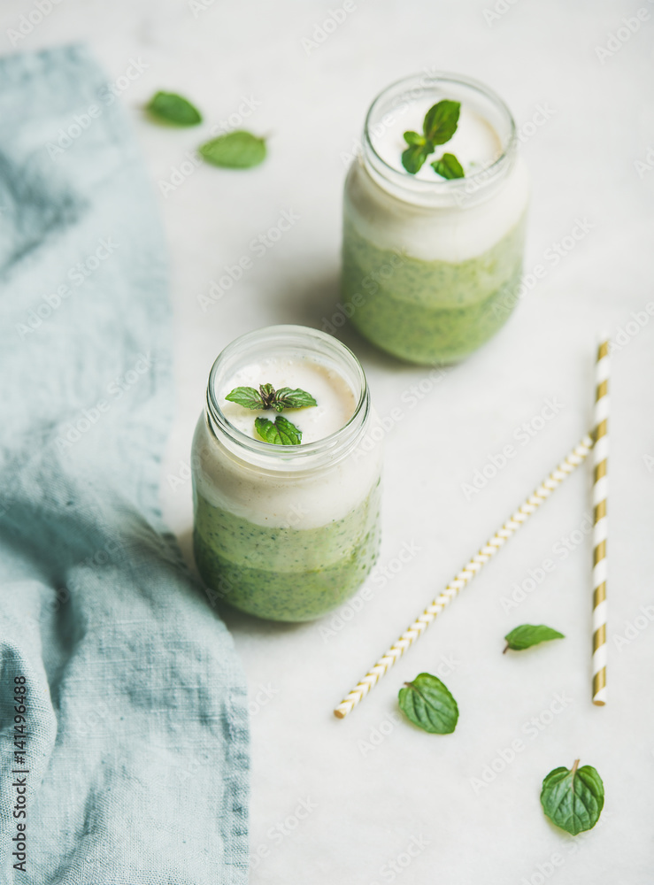 Ombre layered green smoothies with mint in glass jars over light grey background, selective focus. C