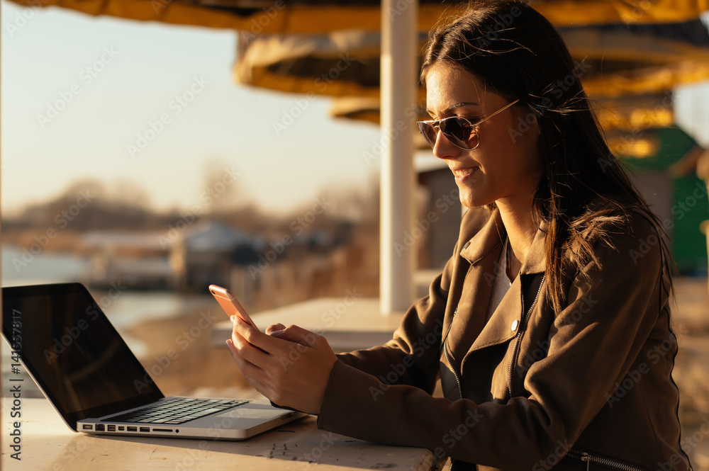 Smiling girl in sunglasses using laptop outdoor