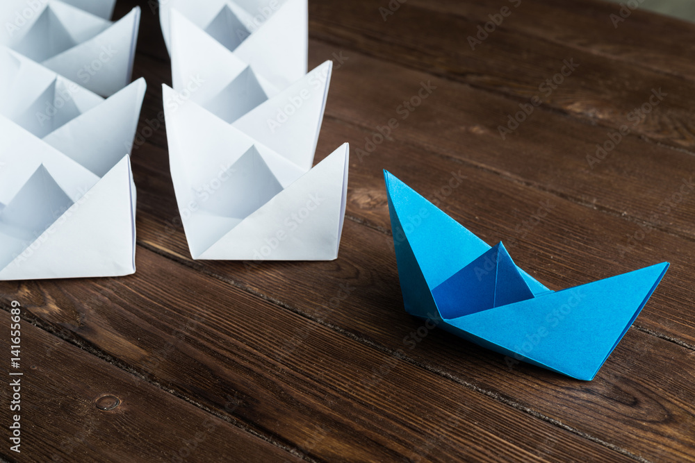 Business leadership concept with white and color paper boats on wooden table