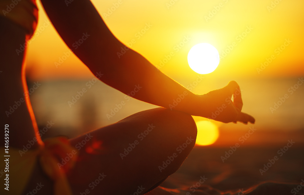 hands of woman meditating in yoga pose at sunset on beach