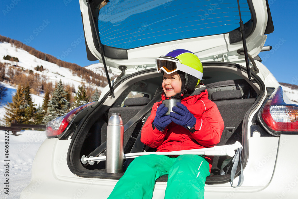 Little skier sitting in car boot and drinking tea