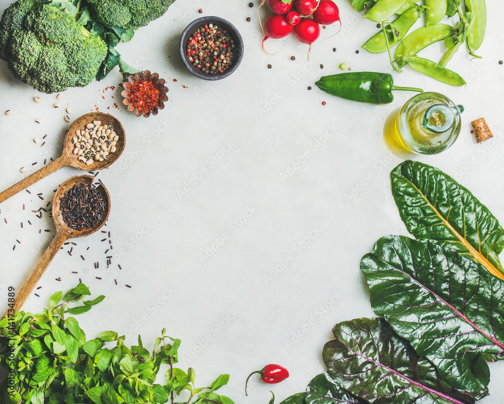 Fresh raw greens, vegetables, olive oil and grains over light grey marble kitchen countertop, top vi