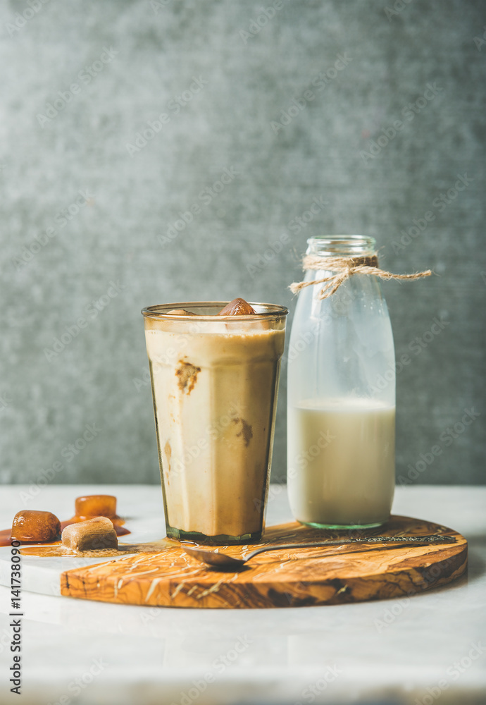 Iced caramel latte summer coffee cocktail with milk and frozen coffee ice cubes in glass on serving 