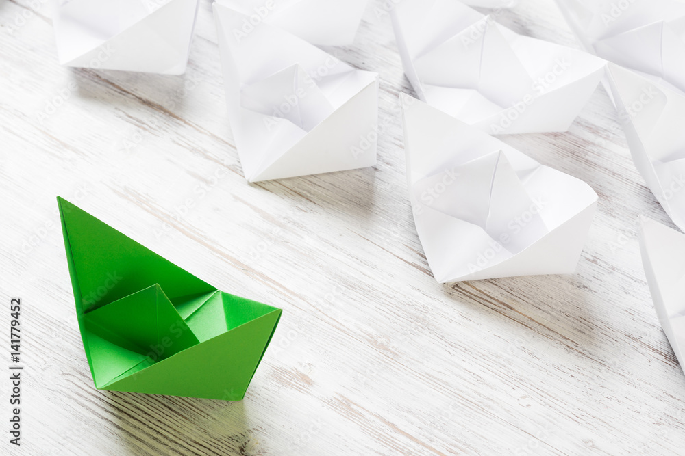 Business leadership concept with white and color paper boats on wooden table