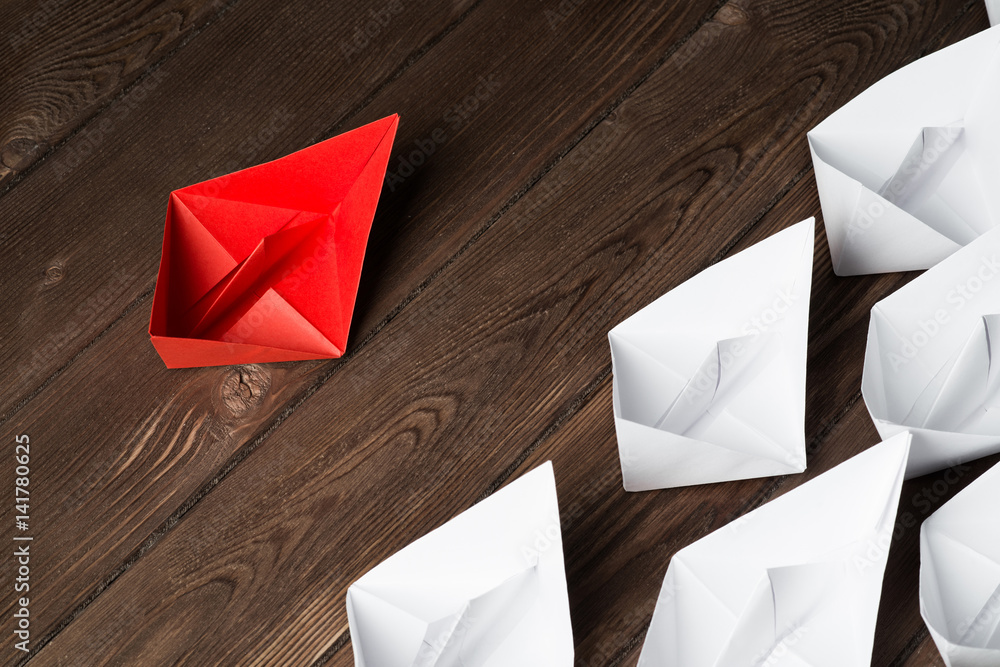 Business leadership concept with white and color paper boats on wooden table