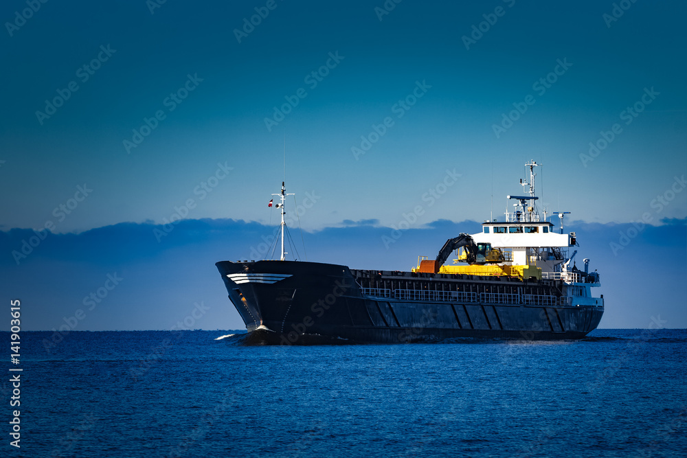 Black cargo ship with long reach excavator moving by baltic sea