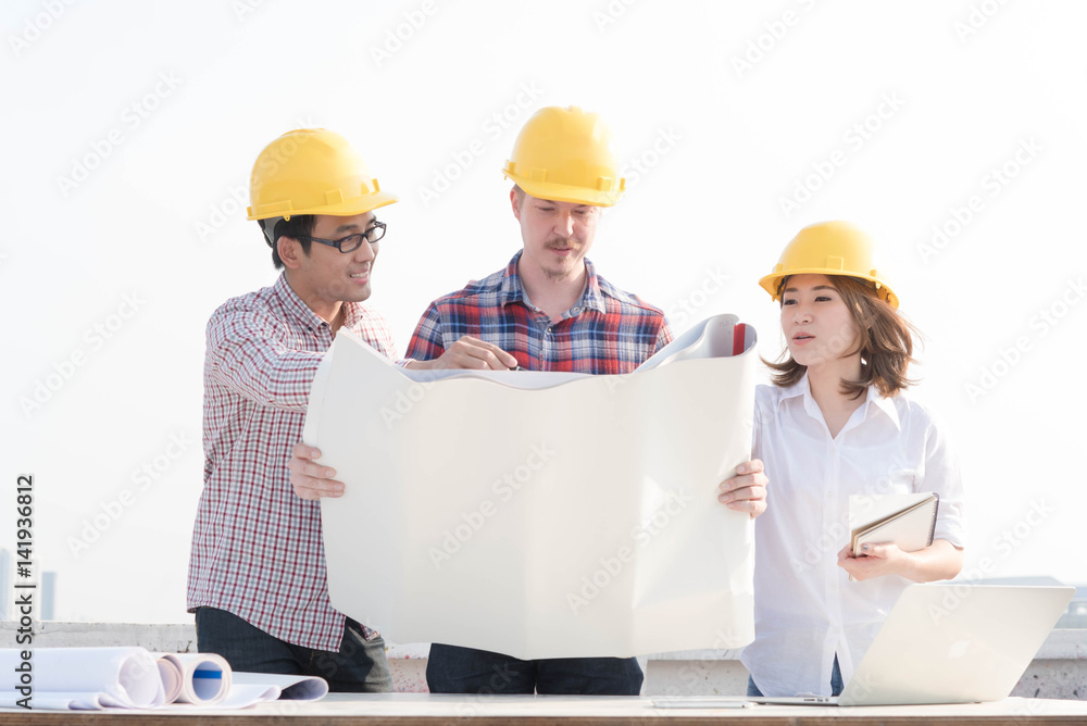 three construction engineers working outdoors in construction site with blueprint on table