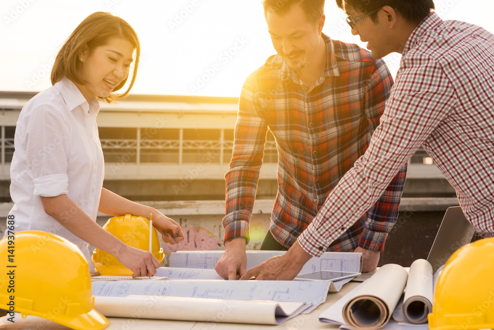 three construction engineers working outdoors in construction site with blueprint on table