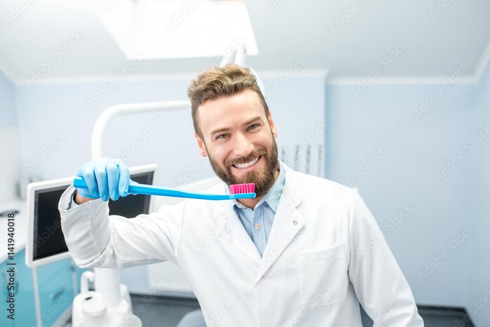 Portrait of funny dentist in uniform with big toothbrush at the dental office