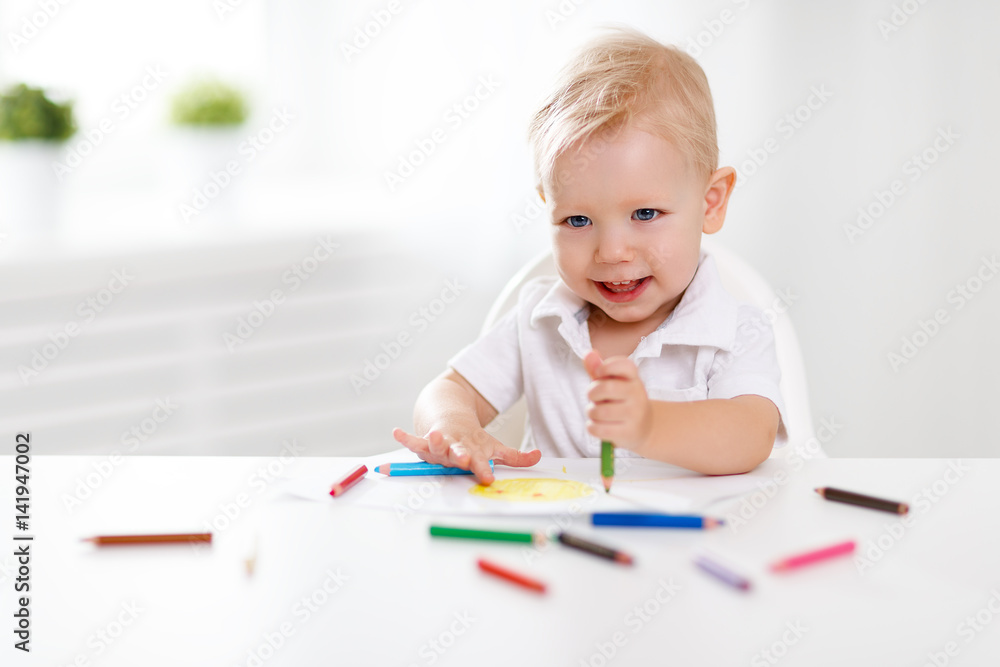 Happy baby boy draws with colored pencils.