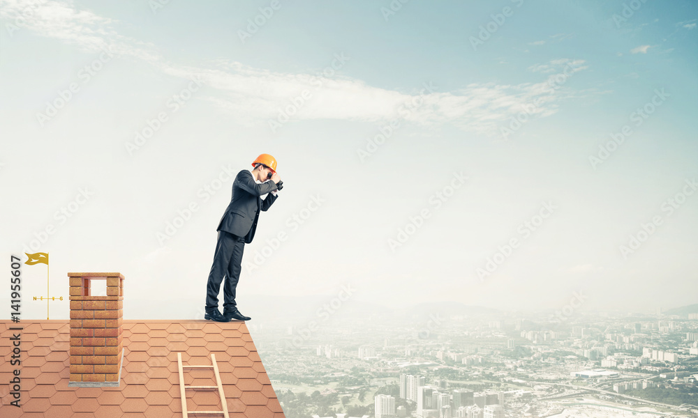 Engineer man standing on roof and looking in binoculars. Mixed m