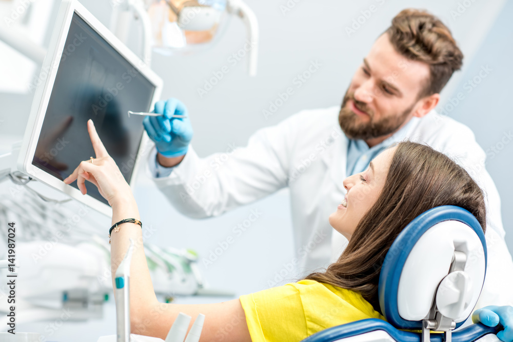 Dentist showing young woman patient tooth x-ray on the monitor at the dental office