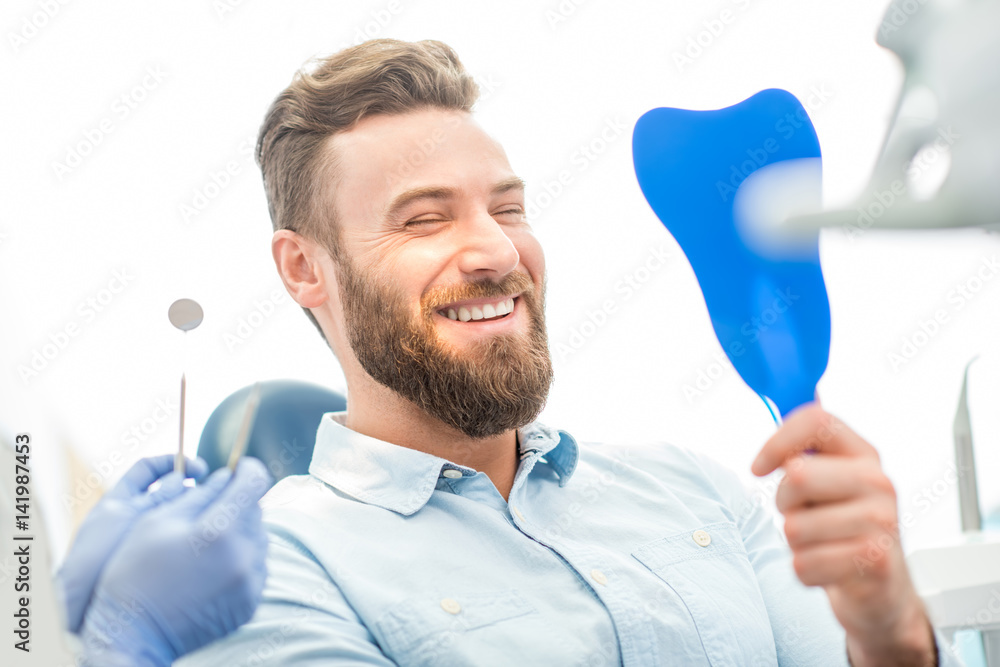 Handsome male patient looking at his beautiful smile sitting at the dental office