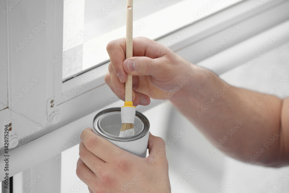 Hands of young worker painting window in office