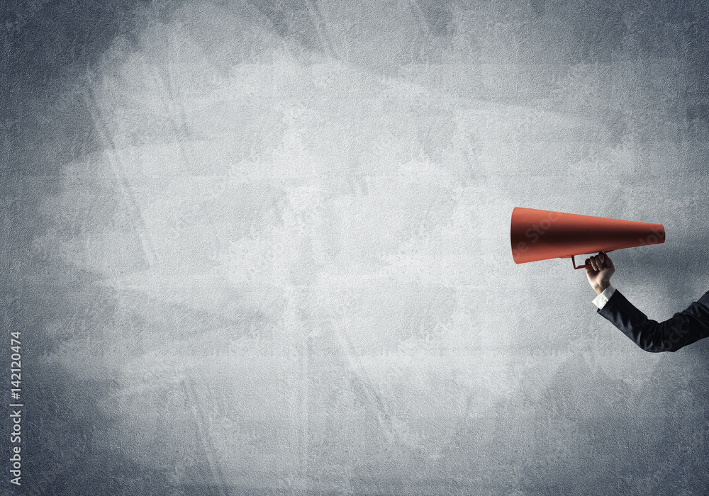 Hand of businesswoman holding red paper trumpet against concrete background