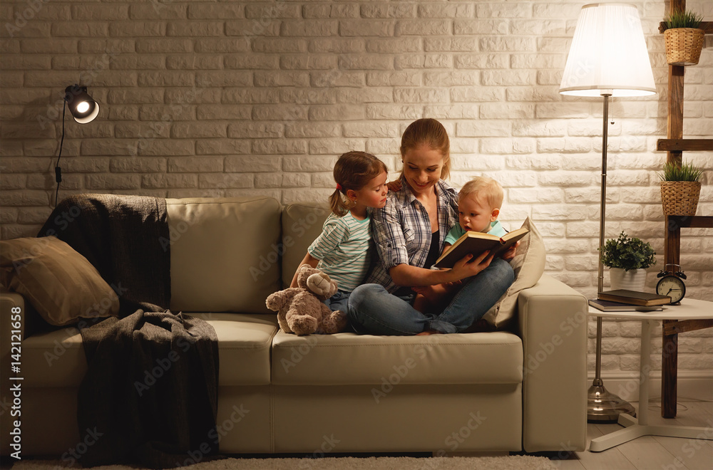 Family before going to bed mother reads children book about lamp in evening