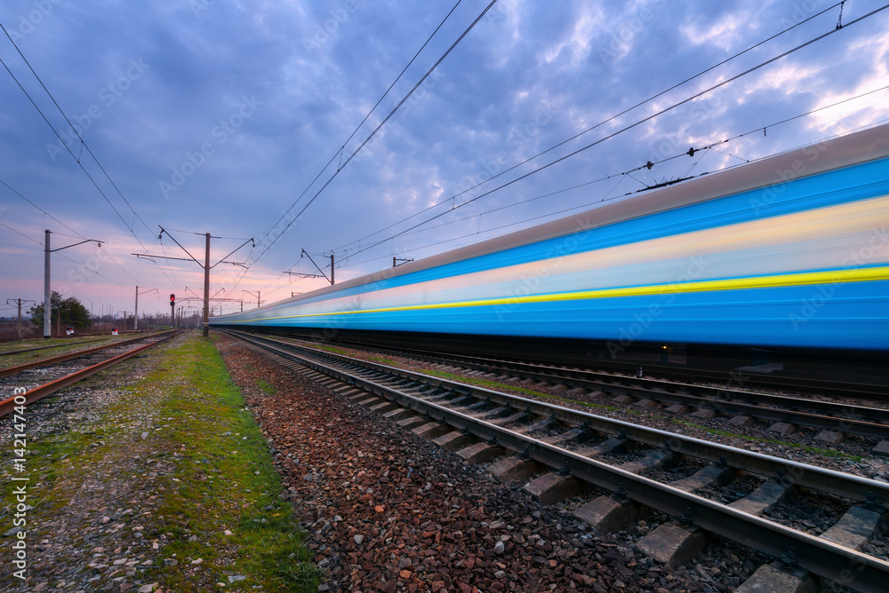 High speed blue passenger train in motion on railroad at sunset. Blurred commuter train. Railway sta