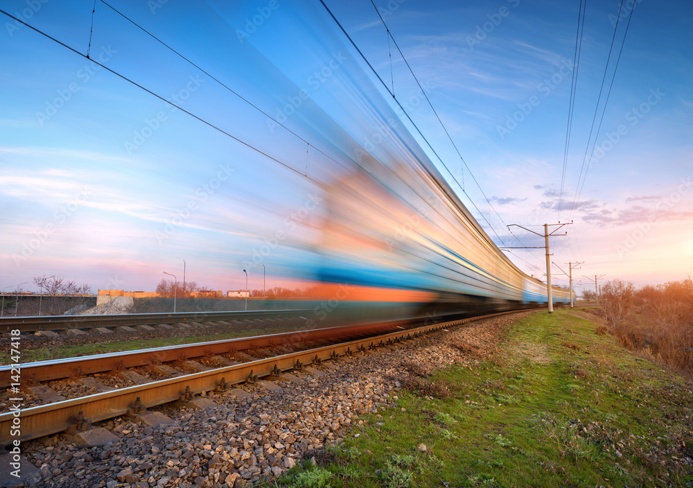 High speed passenger train in motion on railroad at sunset. Blurred commuter train. Railway station 