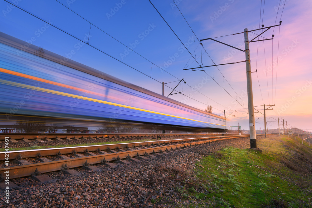 High speed passenger train in motion on railroad at sunset. Blurred commuter train. Railway station 