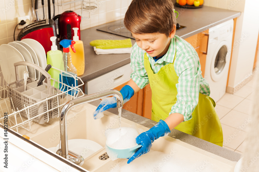 Nice boy wash dish in sink under water from tap