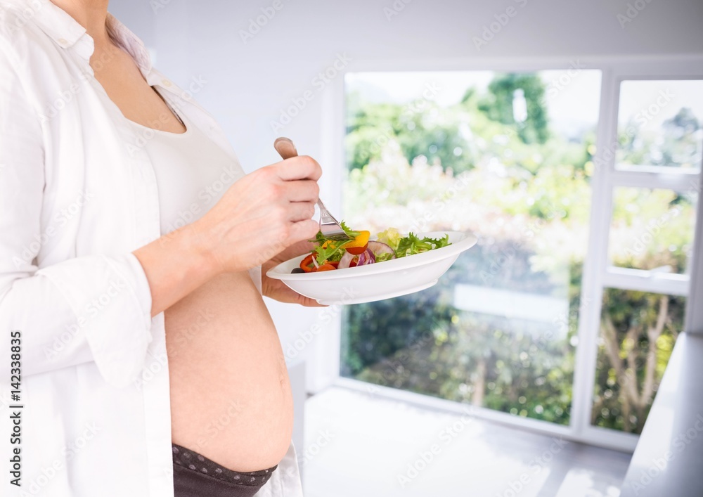 Pregnant woman mid section holding salad in blurry kitchen