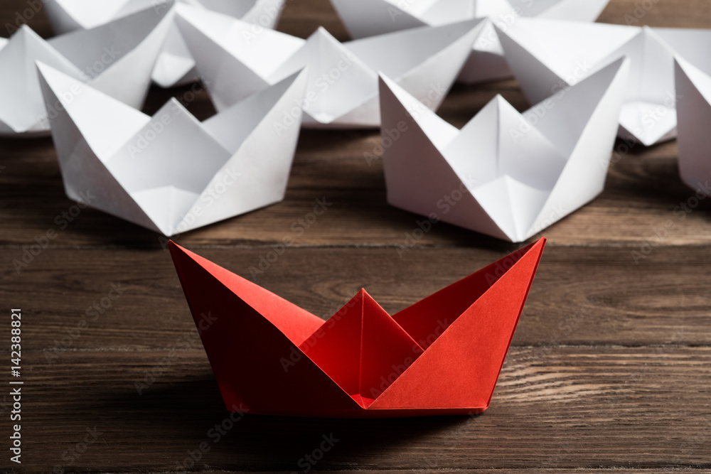 Business leadership concept with white and color paper boats on wooden table