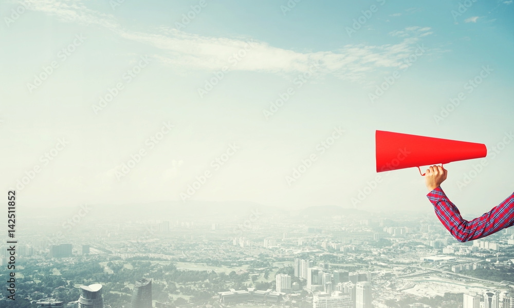 Hand of woman holding red paper trumpet against cityscape background