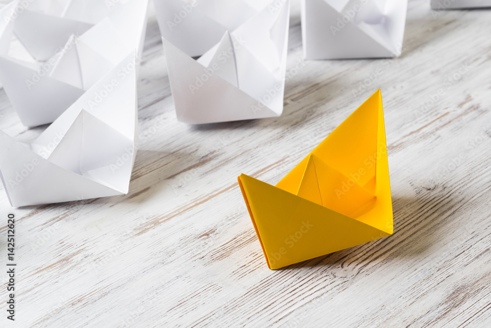 Business leadership concept with white and color paper boats on wooden table