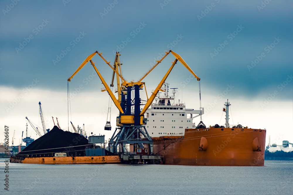 Large orange cargo ship loading with a coal in the port