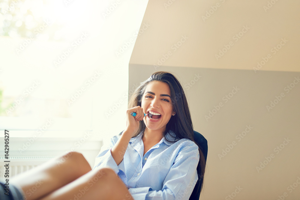 Beautiful young woman brushing teeth in office