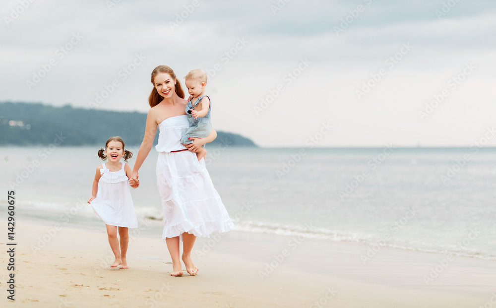 Happy family mother and children on beach by sea in summer