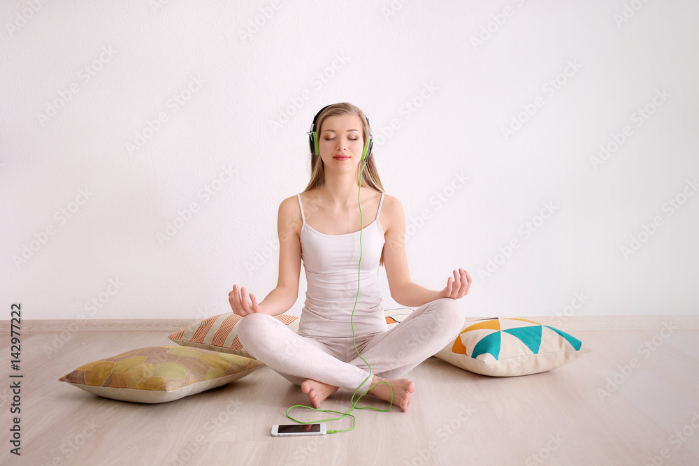 Young woman meditating and listening to music while sitting on floor at home