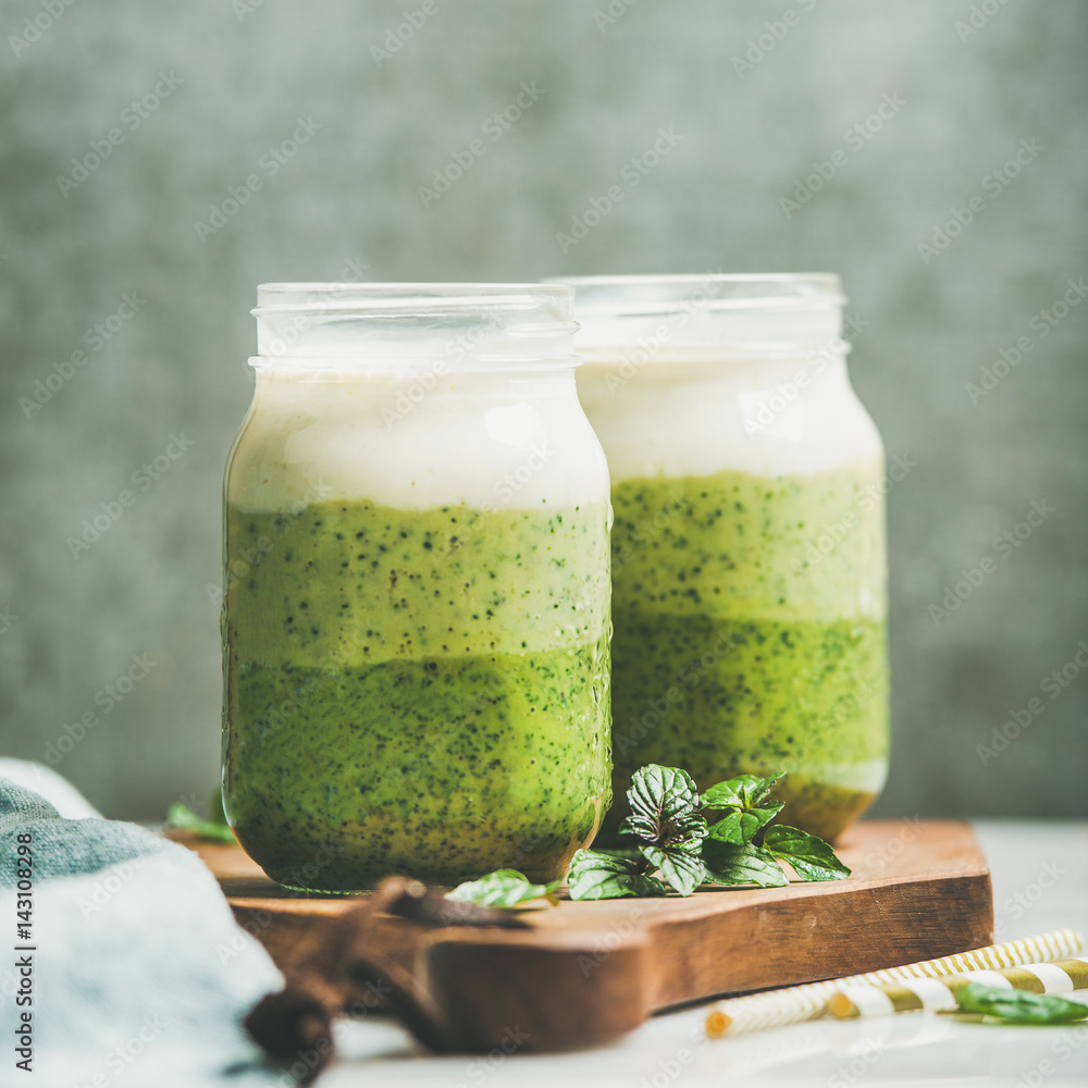 Ombre layered green smoothies with mint in glass jars, grey concrete wall background, copy space, se