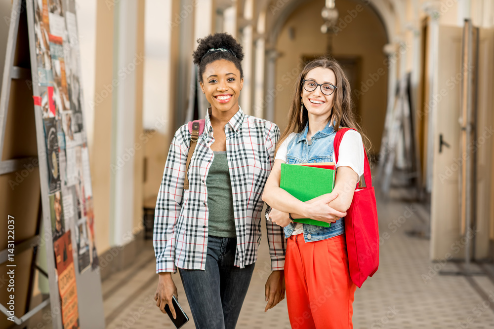 Portrait of a young female multiethnicity students standing together at the old university corridor