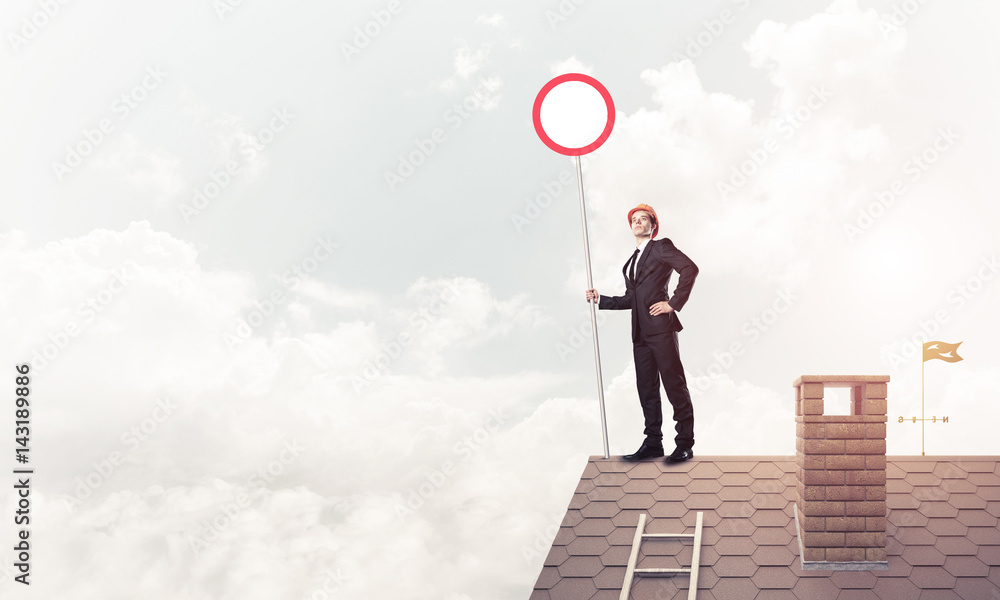 Caucasian businessman on brick house roof showing stop road sign