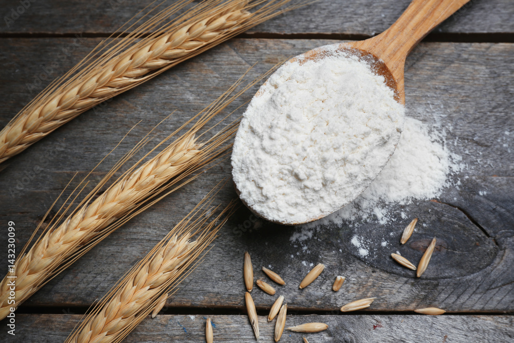 Spoon with flour and wheat on wooden table