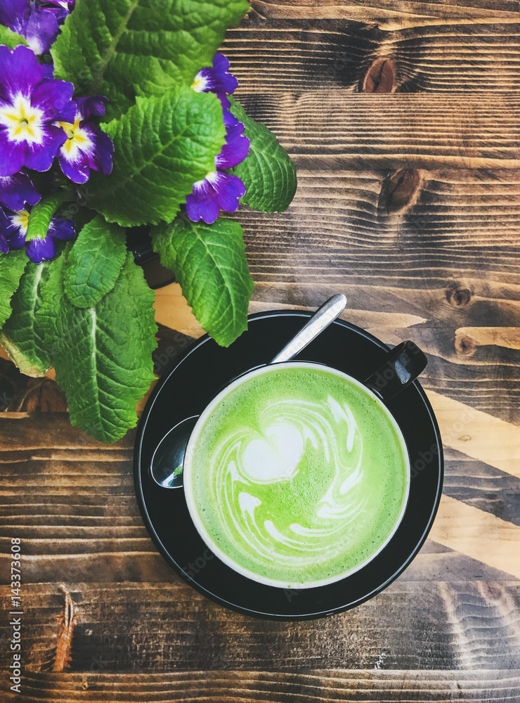 Cup of matcha latte and bright flowers on wooden table, top view, vertical composition