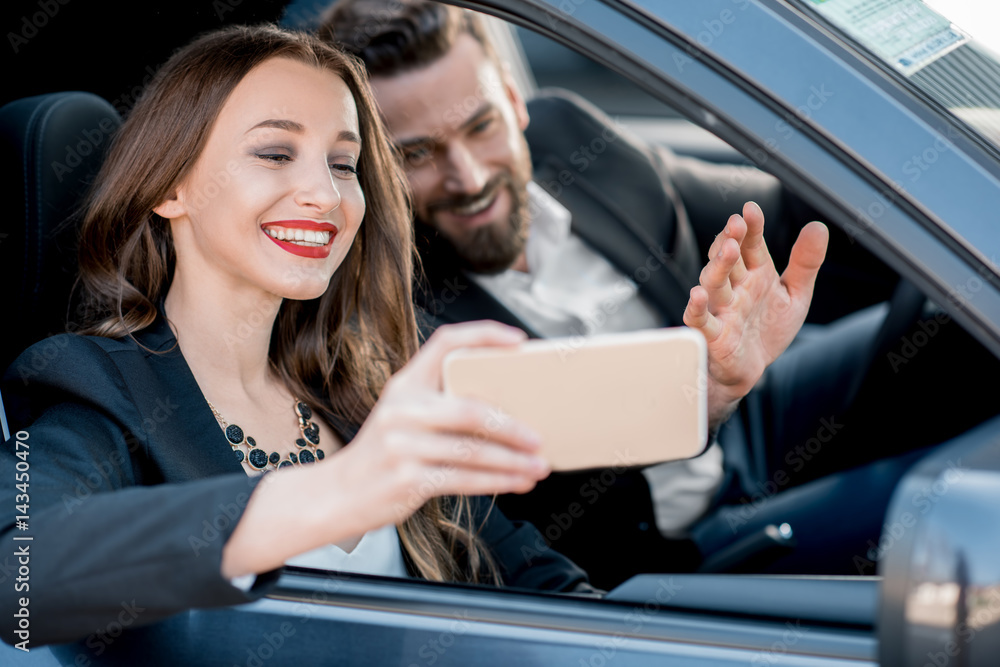 Beautiful businesswoman making selfie portrait with elegant driver sitting in the car