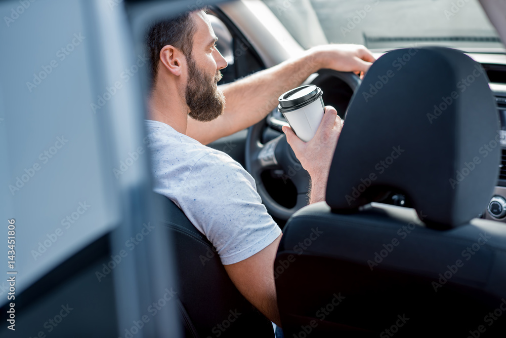 Handsome man dressed cassual in white t-shirt driving a car with coffee to go