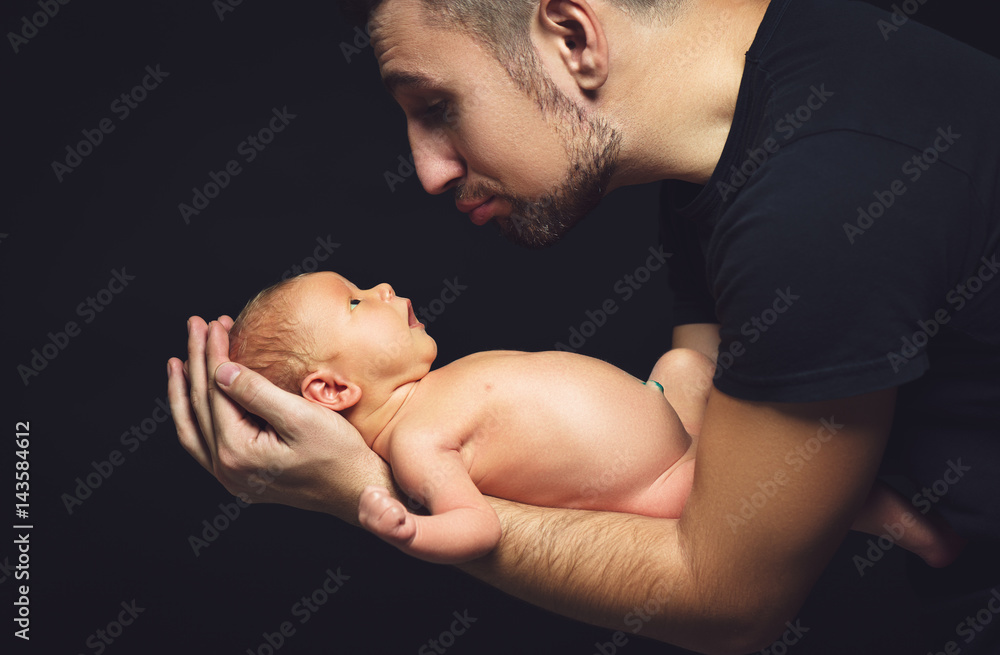 Newborn baby in his fathers hands in dark