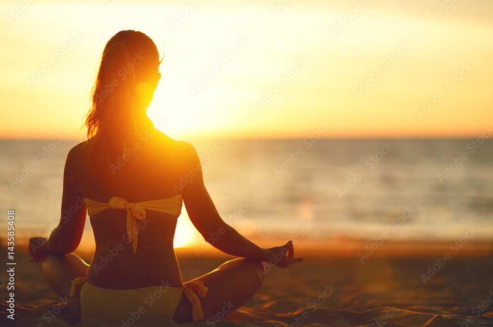 woman practices yoga and meditates in lotus position on beach