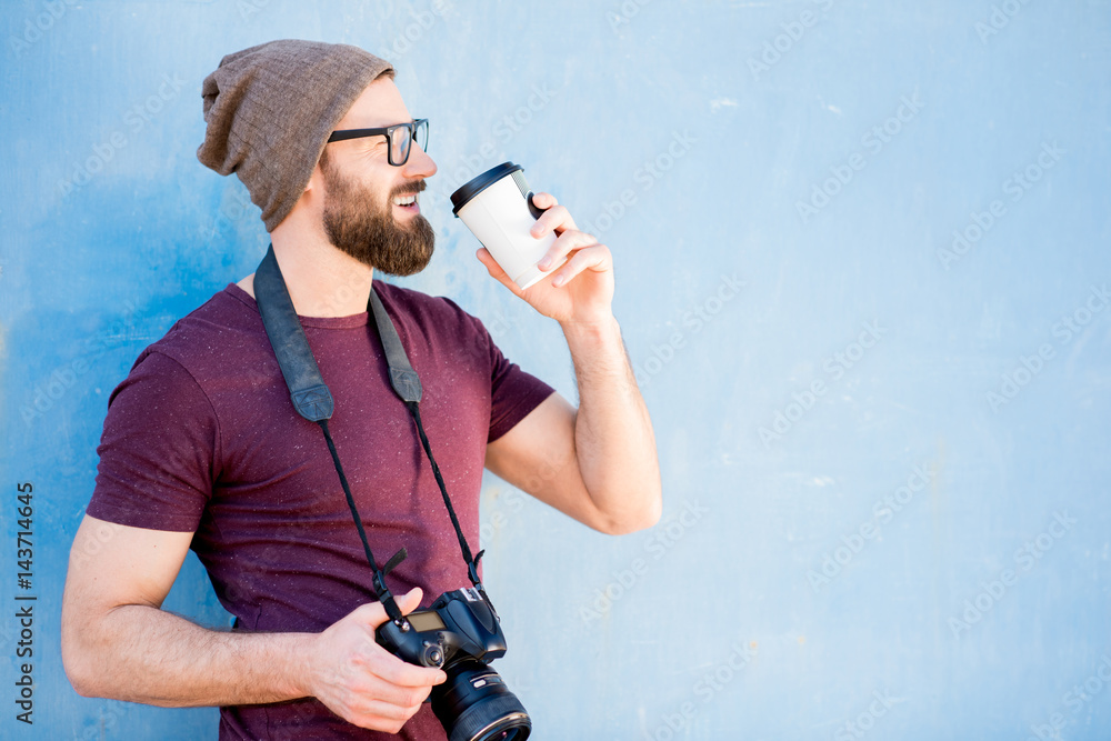 Portrait of a stylish photographer dressed casual in t-shirt and hat standing with camera and coffee