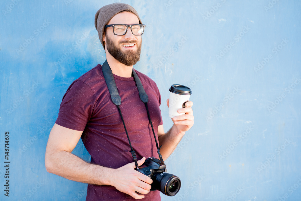 Portrait of a stylish photographer dressed casual in t-shirt and hat standing with camera and coffee