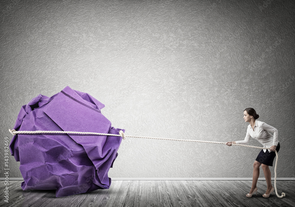 Woman pulling with effort big crumpled ball of paper as creativity sign