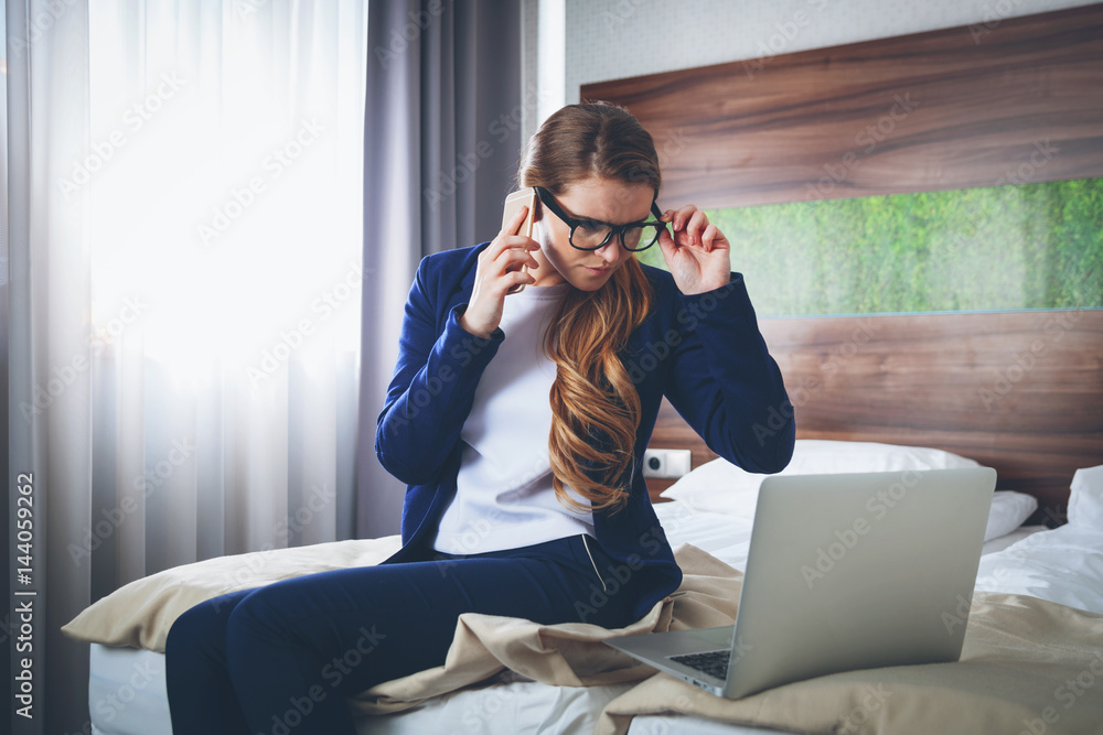 Business woman with suitcase in modern hotel room using laptop and smartphone